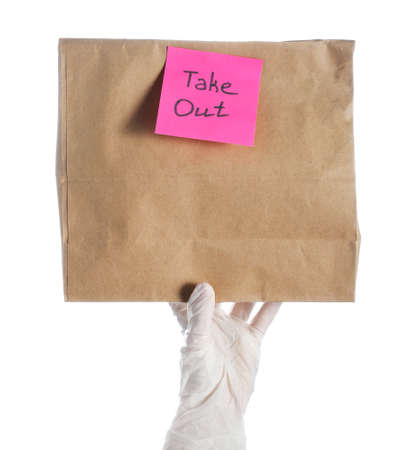 Female hand in medical glove with paper bag and sticker TAKE OUT on white background