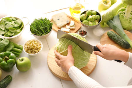 Woman cutting cabbage on table in kitchenの写真素材