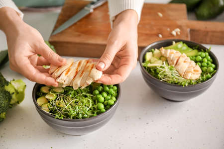 Woman making tasty salad with fresh vegetables and chicken on light background