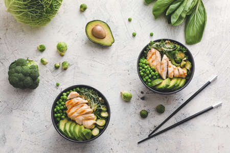 Bowls of tasty salad with fresh vegetables and chicken on light backgroundの写真素材