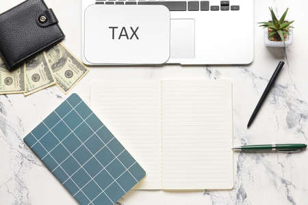 Laptop with wallet, money, notebooks and word TAX on white backgroundの写真素材