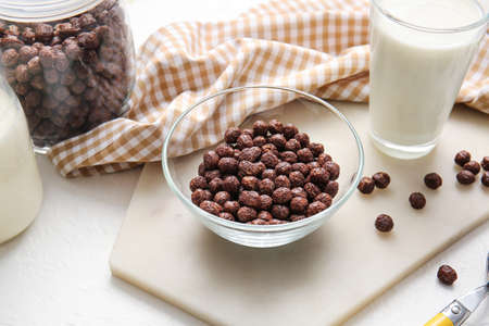Bowl with chocolate corn balls and glass of milk on light background