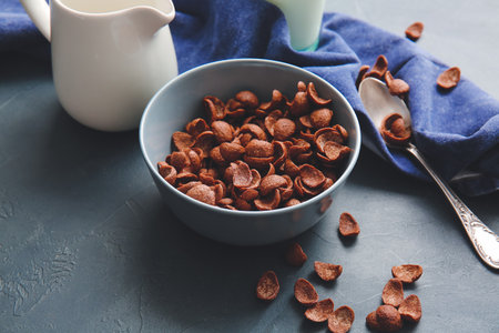 Bowl with chocolate cornflakes and jug of milk on dark backgroundの写真素材