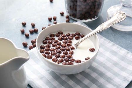 Bowl with chocolate corn balls and milk on color background