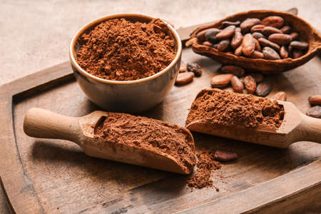 Bowl and scoops with cocoa powder and beans on wooden background