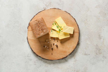 Wooden board with fresh butter and bread on light backgroundの写真素材