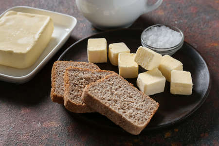 Plate with fresh butter, bread and salt on grunge background
