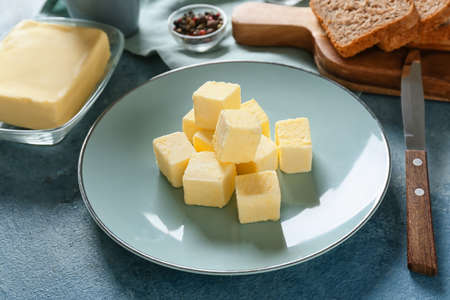 Plate with fresh butter on color background