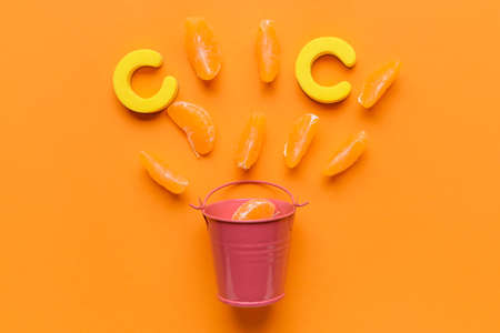 Letters C and bucket with mandarin pieces on color backgroundの写真素材