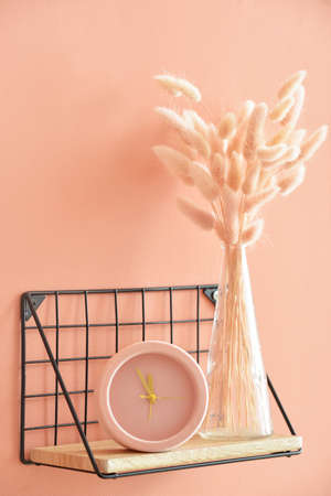 Modern shelf with alarm clock and vase on color wall