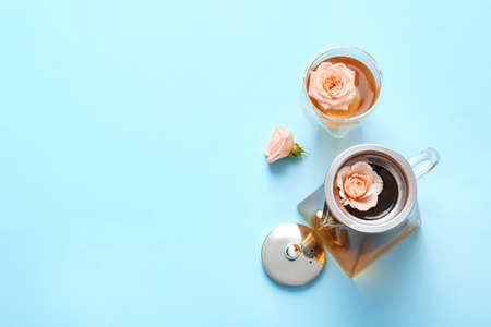 Teapot with hot tea, glass and rose flowers on color background