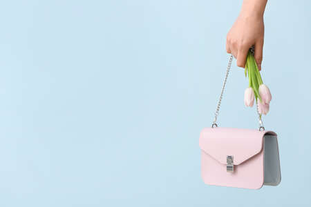 Hand with bouquet of beautiful flowers and bag on color backgroundの写真素材