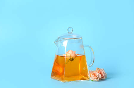 Teapot with hot tea and rose flowers on color backgroundの写真素材