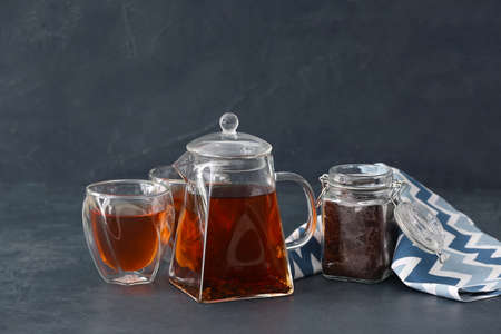 Teapot with hot tea, glasses and dry leaves on dark backgroundの写真素材