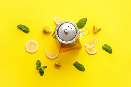 Teapot with hot tea, rose flowers, lemon and mint on color backgroundの写真素材