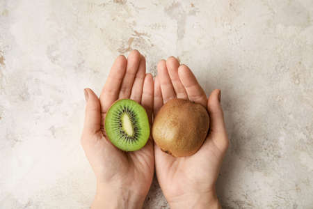 Female hands with fresh kiwi fruit on grunge backgroundの写真素材
