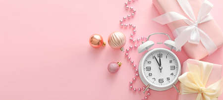 Alarm clock with gifts and Christmas decorations on pink background with space for textの写真素材