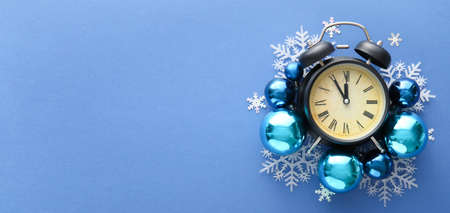 Alarm clock with Christmas decorations on blue background with space for text