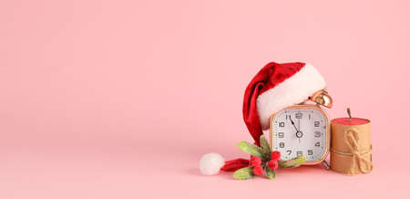 Alarm clock with Santa hat and candle on pink background with space for textの写真素材