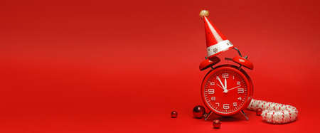 Alarm clock with party hat and Christmas decorations on red background with space for textの写真素材