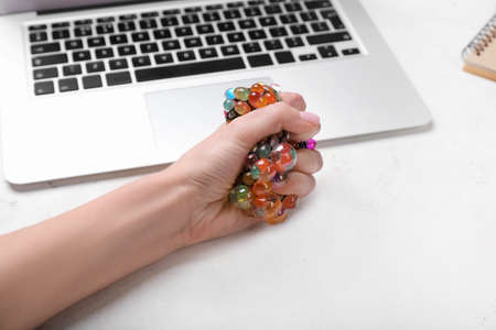 Woman squeezing stress ball while working with laptop in officeの写真素材