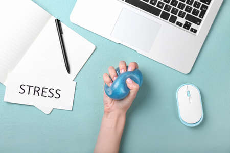 Woman squeezing stress ball while working with laptop in officeの写真素材