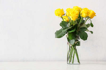 Vase with beautiful yellow roses on table against light backgroundの写真素材