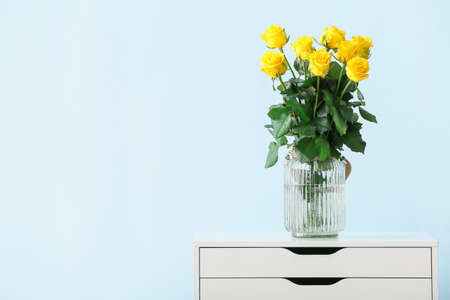 Vase with beautiful yellow roses on table against color backgroundの写真素材