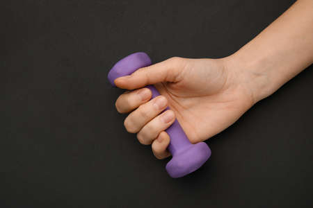 Female hand with dumbbell on dark background