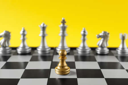 Golden pawn standing out from silver chess pieces on color backgroundの写真素材