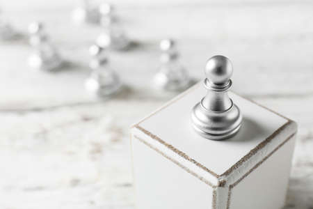 Silver pawn standing out from others on white wooden background, closeupの写真素材