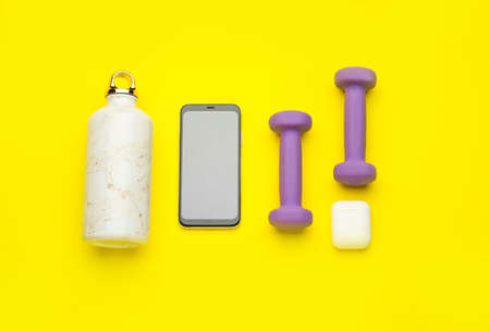 Dumbbells, gadgets and bottle of water on yellow backgroundの写真素材