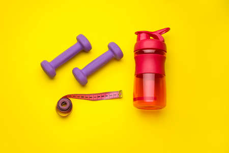 Dumbbells, measuring tape and bottle of water on yellow backgroundの写真素材
