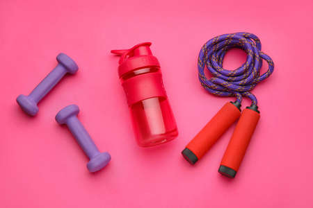 Dumbbells, skipping rope and bottle of water on pink backgroundの写真素材