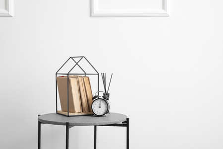 Bedside table with books, alarm clock and reed diffuser near white wall