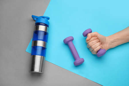 Female hand with dumbbells and bottle on color backgroundの写真素材
