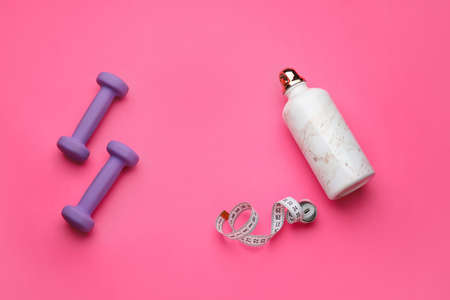 Dumbbells, bottle of water and measuring tape on pink backgroundの写真素材