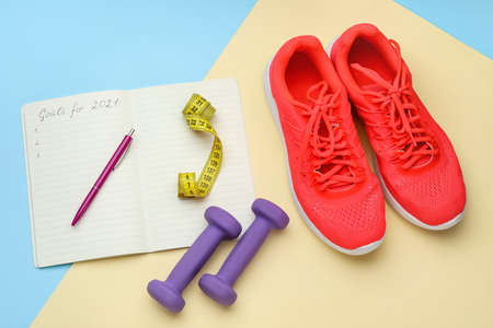 Dumbbells, shoes and notebook with text GOALS FOR 2021 on color backgroundの写真素材