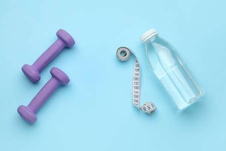 Dumbbells, measuring tape and bottle of water on blue backgroundの写真素材