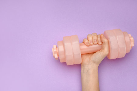 Female hand with dumbbell on purple backgroundの写真素材