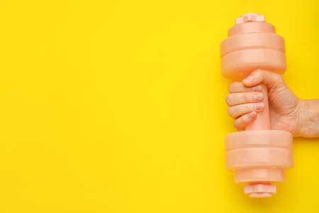 Female hand with dumbbell on yellow background