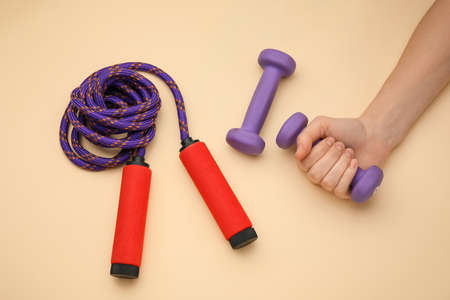 Female hand with dumbbells and skipping rope on beige backgroundの写真素材