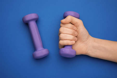 Female hand with dumbbells on blue backgroundの写真素材