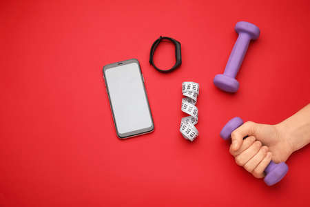Female hand with dumbbells, gadgets and measuring tape on red backgroundの写真素材