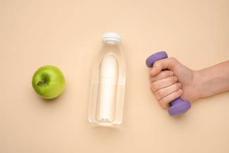 Female hand with dumbbell, bottle of water and apple on beige backgroundの写真素材