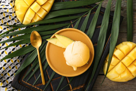 Plate with tasty mango ice cream and palm leaf on wooden backgroundの写真素材