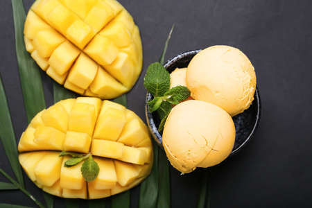 Bowl with tasty mango ice cream and palm leaf on dark backgroundの写真素材