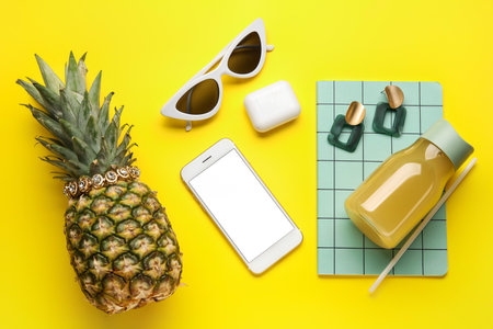 Pineapple with female accessories, bottle of juice, mobile phone and stationery on color backgroundの写真素材