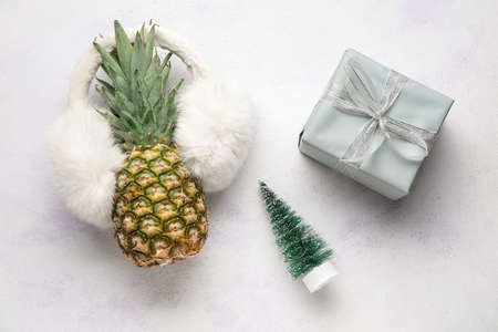 Pineapple with ear warmers, fir tree and gift box on white backgroundの写真素材