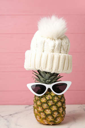 Pineapple with sunglasses and knitted hat on table